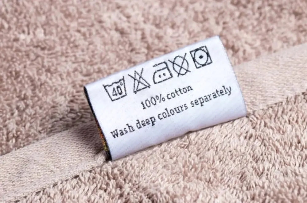 Wash care instruction label attached to 100% cotton towel fabric.