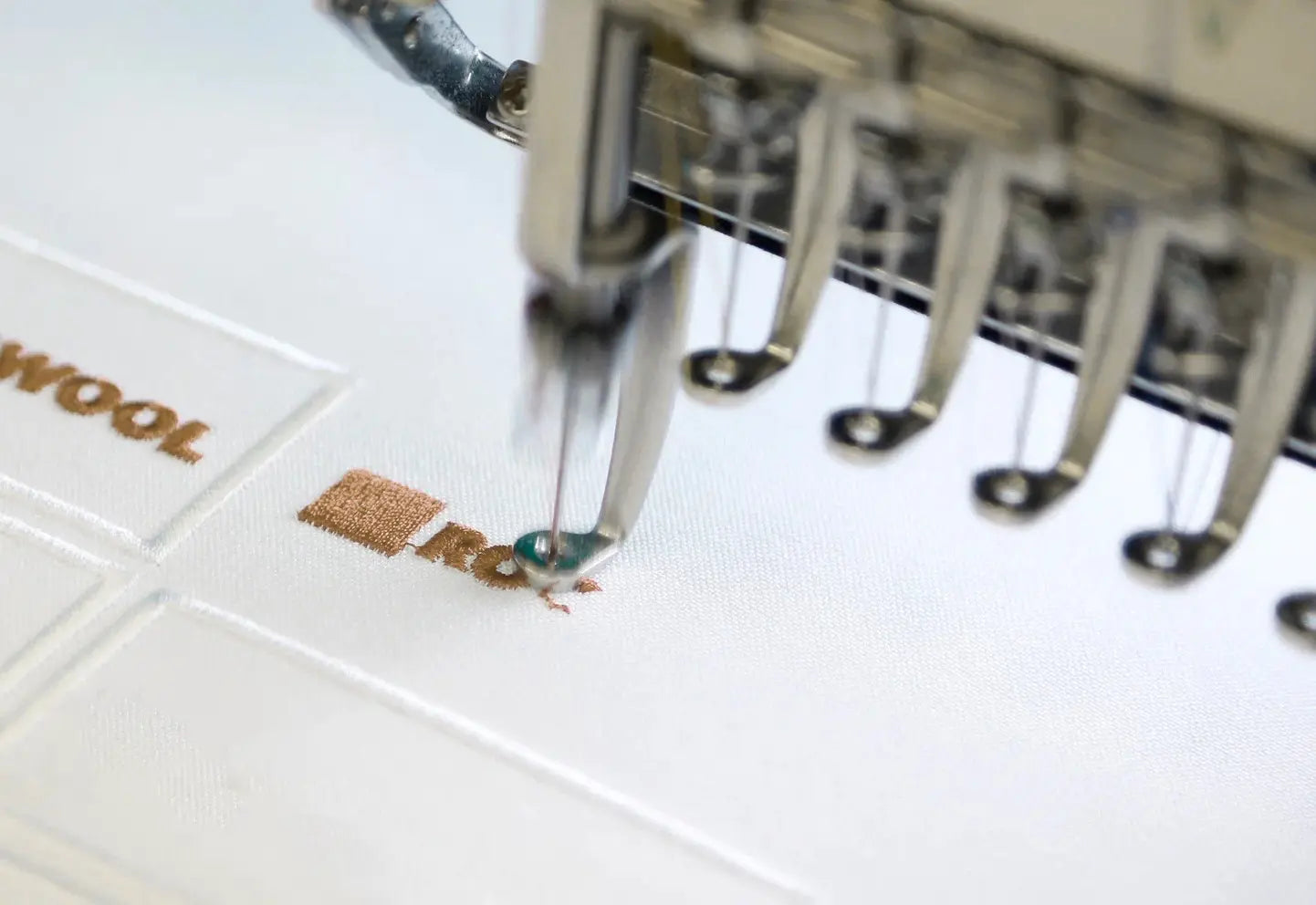 Close-up of embroidery machine stitching custom monogram on white pillow cover