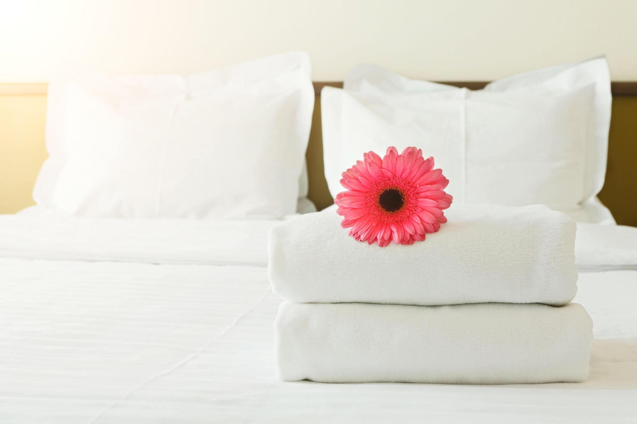 Luxury white hotel towels folded on a bed with pillows and flower decoration.