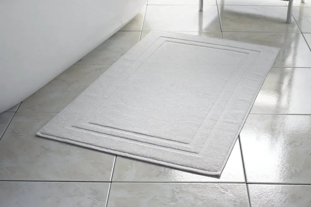 White bath mat placed on bathroom floor tiles